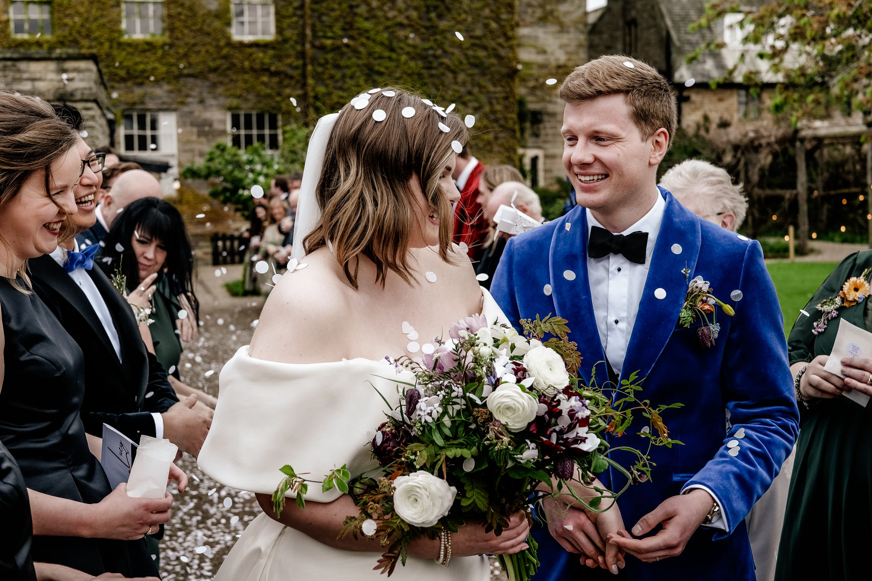 Bride and groom in a confetti shower. Bride wears an Eva Mendel dress and carries a bouquet by Moonwind Flowers. Sneaton Castle wedding, Whitby.